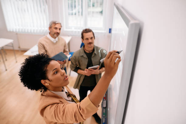 istock Black female teacher writing on whiteboard while giving lecture in the classroom. 1349170279