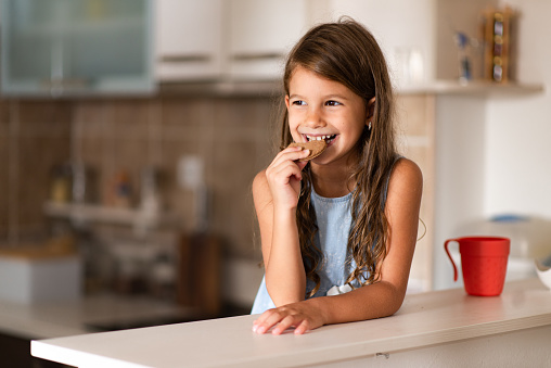 Beautiful girl in kitchen eating cookie.
