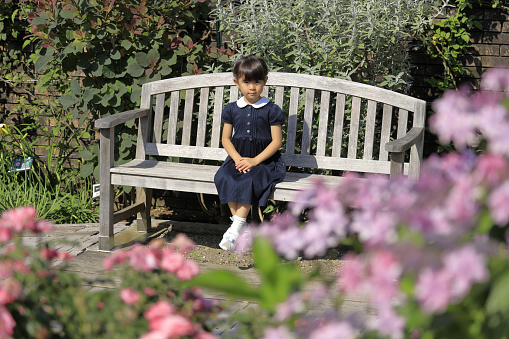 Japanese student girl sitting on the bench in flower bed (6 years old)