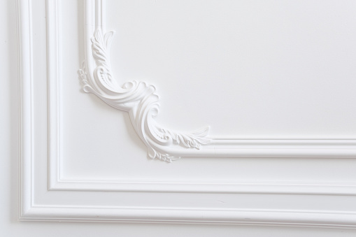 Plaster molding is a decorative decoration of a white wall in a classic style. White wall in the room with baroque elements. Space for text.