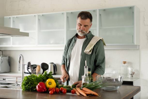 istock Handsome senior man cooking at home preparing salad in kitchen 1349177395