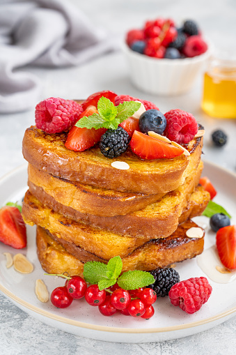 A stack of French toast on a plate with fresh berries, almond petals and honey on a gray concrete background. Delicious breakfast. Copy space