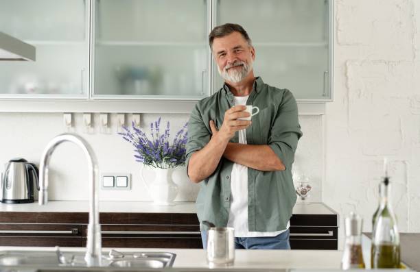 szczęśliwy dojrzały mężczyzna pijący kawę w domu w kuchni, cieszący się gorącym napojem rano w weekend. - 60s senior adult breakfast cheerful zdjęcia i obrazy z banku zdjęć