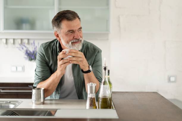szczęśliwy dojrzały mężczyzna pijący kawę w domu w kuchni, cieszący się gorącym napojem rano w weekend. - 60s senior adult breakfast cheerful zdjęcia i obrazy z banku zdjęć