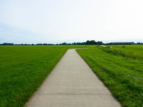 Long distance bicycle road through dutch landscape,\nNarrow asphalt road between meadows.