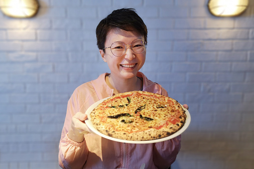 An Asian woman is showing a full plate of pizza in restaurant.