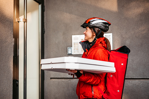 Delivery woman entering residential building with two boxes with pizza.