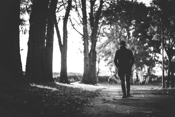 Portrait of a handsome young male model wearing black hat and long black coat, he is walking in autumn public park.