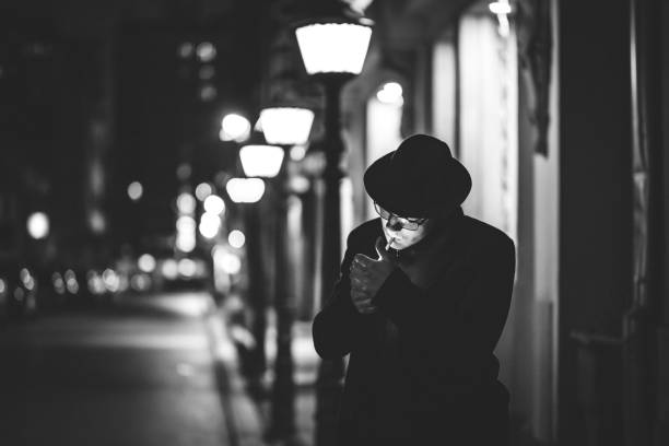 homem bonito com chapéu acendendo cigarro na rua da cidade - street light dark street men - fotografias e filmes do acervo
