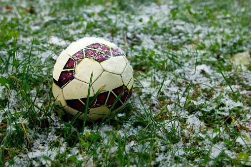 Small soccer ball on green grass covered with fresh snow
