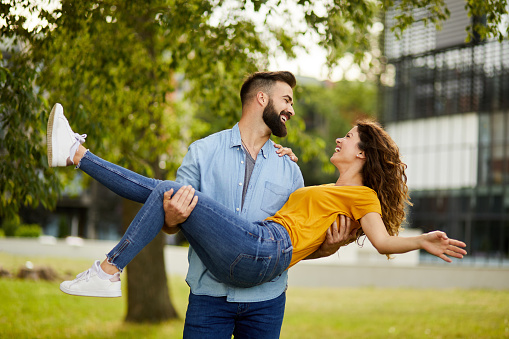 Man carrying his girlfriend in arms, spinning her around in the park