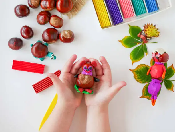 Photo of In children's hands, a ready-made craft made of natural material, a bear made of chestnuts and plasticine.