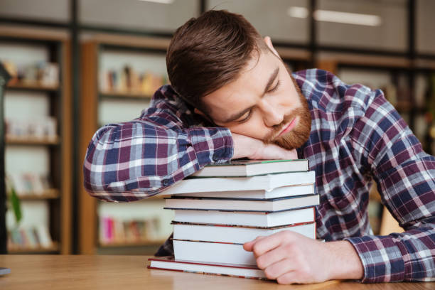 istock Tired young man holding his head on the book stack 1349196882
