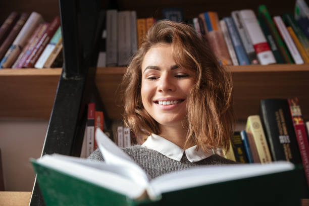 istock Smiling student girl reading book at library 1349197699