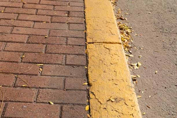 istock Red brick sidewalk edged in concrete curb painted bright yellow, muddy asphalt road bed 1349199185