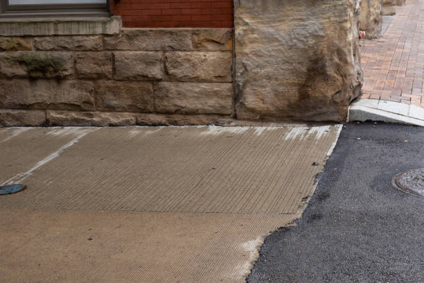 istock Corner of a red brick and rusticated stone building meeting a brick sidewalk, concrete driveway, and asphalt road surface 1349199217