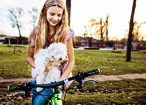 Cute blond girl sitting on a bicycle and holding her dog