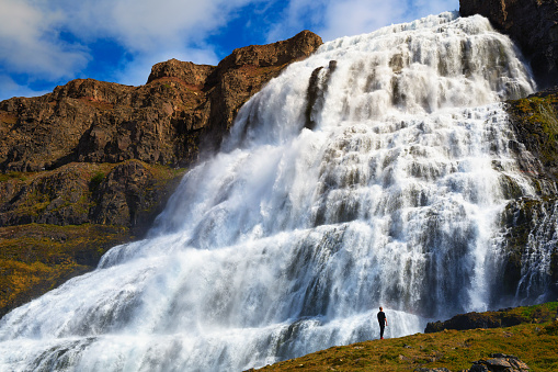 Person standing at the Dynjandi waterfall, also known as Fjallfoss, located on the Westfjords peninsula in northwestern Iceland.