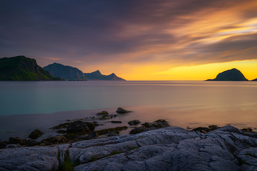 Dramatic sunset over the mountains and the sea of Lofoten islands in Norway with rocky beach in the foreground, photographed from Haukland Beach. Long exposure.