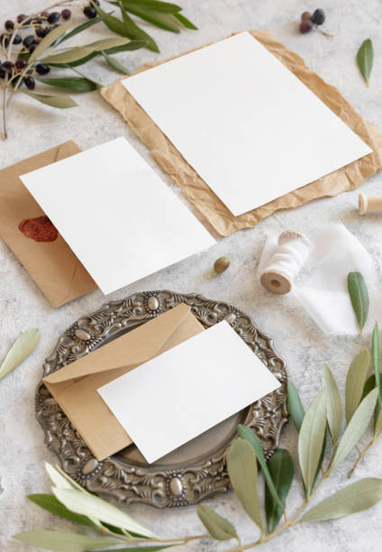 Wedding invitation cards and envelopes on a marble table decorated with olive branches close up. Elegant modern template with paper cards set. Mediterranean flat lay mockup of wedding suite