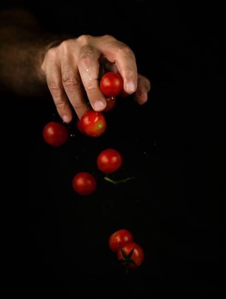 istock Hand dropping cherry tomatoes against black background 1349205516