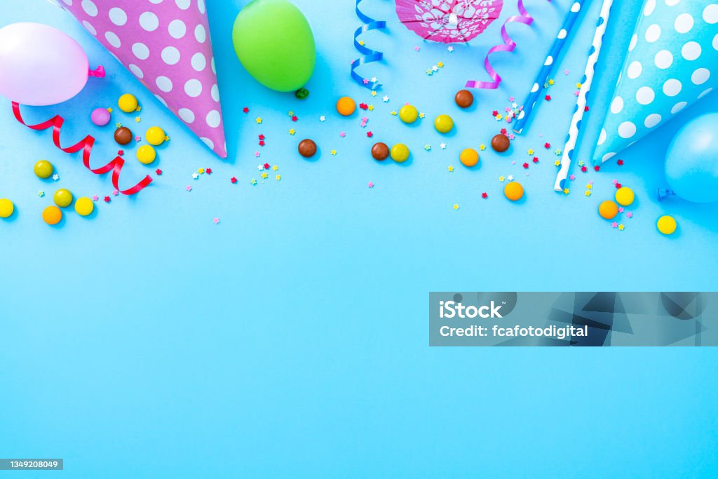 Multicolored party or birthday accessories frame Party or carnival backgrounds. Overhead view of multi colored accessories like balloons, confetti, candies, party hat and drinking straws shot at the top of a blue background making a frame and leaving useful copy space for text and/or logo. High resolution 42Mp studio digital capture taken with SONY A7rII and Zeiss Batis 40mm F2.0 CF lens Birthday Stock Photo