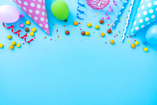 Multicolored party or birthday accessories frame Party or carnival backgrounds. Overhead view of multi colored accessories like balloons, confetti, candies, party hat and drinking straws shot at the top of a blue background making a frame and leaving useful copy space for text and/or logo. High resolution 42Mp studio digital capture taken with SONY A7rII and Zeiss Batis 40mm F2.0 CF lens anniversary photos stock pictures, royalty-free photos & images