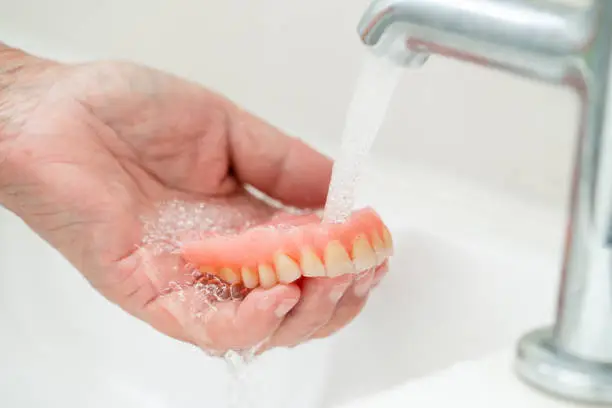 Photo of Asian senior or elderly old woman patient holding and washing denture in nursing hospital ward; healthy strong medical concept