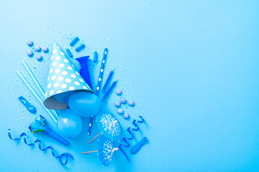 Party or carnival backgrounds. Overhead view of blue colored accessories like balloons, confetti, candies, party hat and streamers shot at the left of a blue background leaving useful copy space for text and/or logo. High resolution 42Mp studio digital capture taken with SONY A7rII and Zeiss Batis 40mm F2.0 CF lens