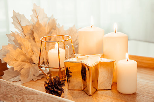 Autumn composition. Candles, golden maple leaves and pine cone on a beige background. Still life with burning candles. Selective focus.