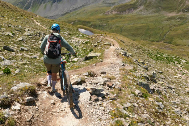 Woman mountain bikes along sunny mountain ridge She follows trail along mountain ridge, in the European Alps top view on people walking and cyclists riding stock pictures, royalty-free photos & images