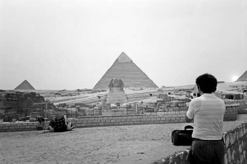 Giza Necropolis: Bedouin men dressed in traditional clothes, ride camels decorated with specific embroidery, in front of the Giza Necropolis pyramids complex.