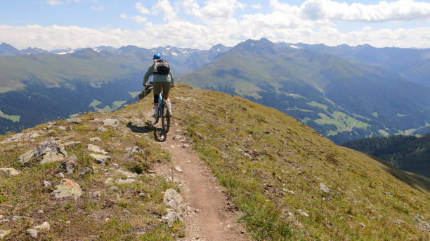 istock Woman mountain bikes along sunny mountain ridge 1349212438