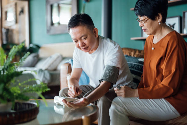 senior asian couple checking blood pressure at home. wife examining blood pressure on her husband's arm with a blood pressure monitor. elderly and healthcare concept - blodtryck orolig bildbanksfoton och bilder