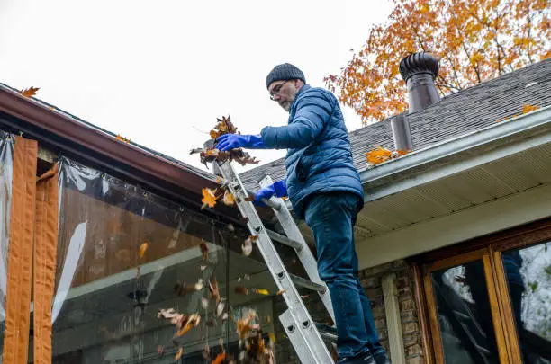 Photo of Man in ladder removing autumn leaves from gutter