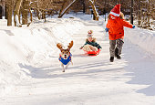 Family have fun with snow on winter day. Kids and dog in Christmas costumes sledding in park