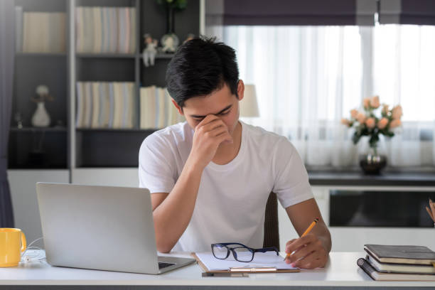 gli uomini asiatici sono stanchi e stressati a lavorare su un laptop e prendere appunti a casa. - financial burden foto e immagini stock