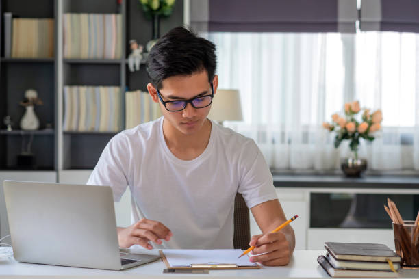 istock Young Asian man is taking notes on the laptop table at home. 1349217434