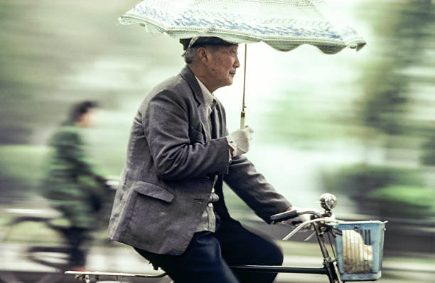 old man rides his bicycle with umbrella in his arm stock photo