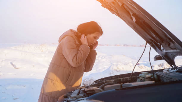 istock Upset woman looks at broken auto engine on snowy road 1349218083