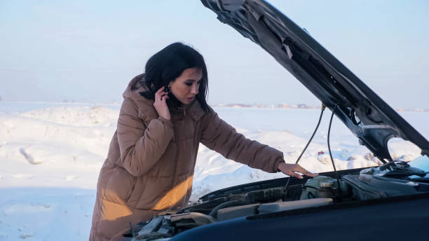 istock Upset woman looks at broken auto engine on snowy road 1349218092