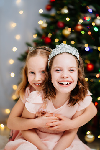 two beautiful and happy little girls in pink dresses at the Christmas tree. the relations of the sisters in the family. Happy New Year. fashionable elegant clothes for girls.