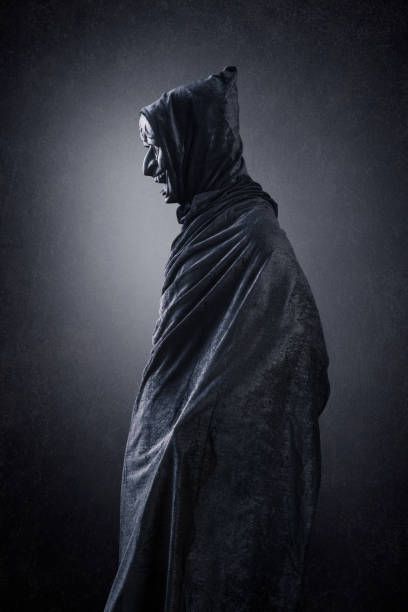 istock Spooky figure with hooded cape over dark misty background 1349220624
