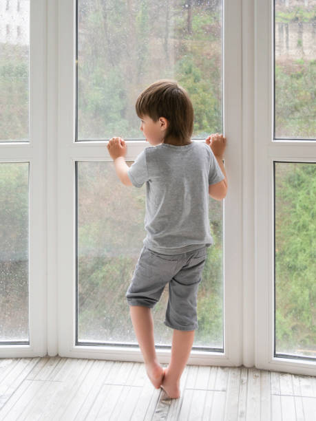 istock Little boy looks outdoors through wet panoramic window with raindrops. Coronavirus COVID19 quarantine. Rainy summer weather. Kid stays alone at home. Loneliness and sad mood without children's company. 1349220704