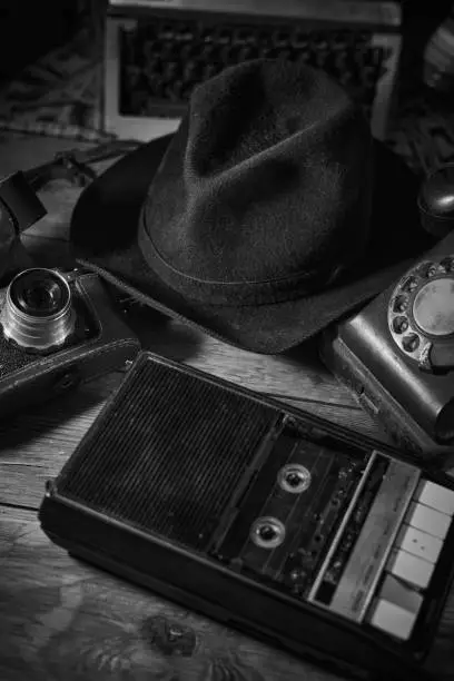 Photo of Old vintage cinematic noir scene, detective's desk with a hat, telephone, camera, portable cassette recorder, and whisky