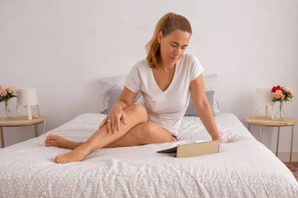 Smiling and casually dressed woman using digital tablet in bed