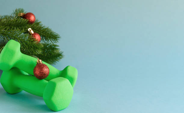 Dumbbells and red Christmas balls on the background of the branches of the Christmas tree. New Year's card for athletes. Blue background with space for text. Selective focus. stock photo
