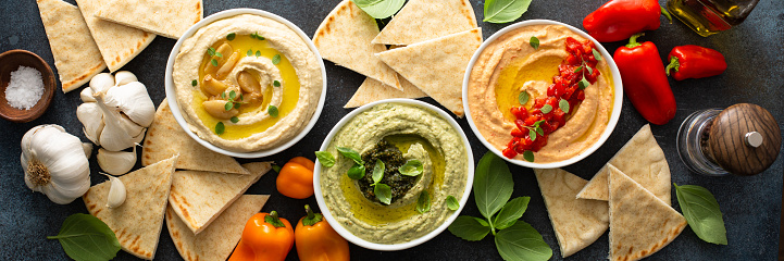 Hummus board with garlic, roasted red pepper and basil variety, served with pita overhead view