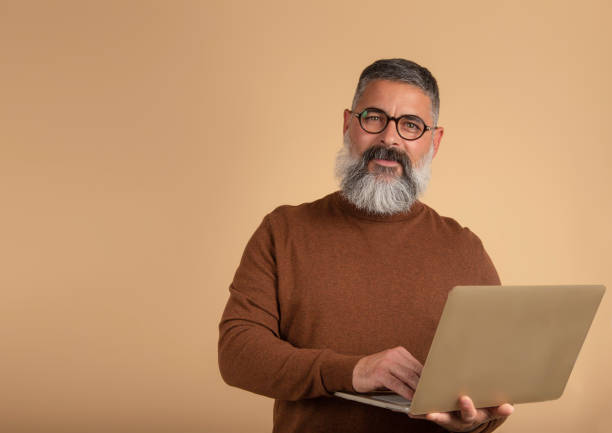 istock image of handsome bearded man on light isolated wall background looking at camera using laptop 1349226402