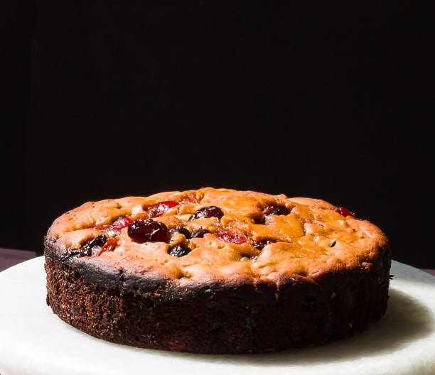 gros plan du gâteau aux fruits de noël placé sur un support de gâteau en marbre blanc et isolé sur fond noir. dessert avec une riche garniture de baies, de noix et de saveur d’orange confite. espace de copie. vue à angle élevé. - fruitcake christmas cake cake raisin photos et images de collection